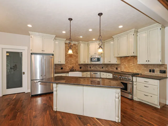 Kitchen featuring wood-finish flooring, an expansive center island with granite countertop, stainless steel appliances, abundant cabinetry, and a stone-tiled backsplash