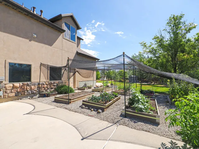 Exterior rear of the property featuring multiple raised garden beds under a shade canopy