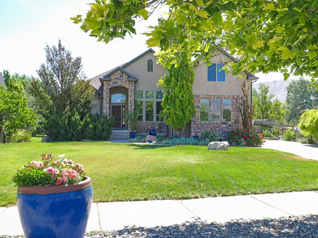 Stucco and stone facade home featuring a prominent arched entryway, large picture windows, mature landscaping, and an expansive lawn