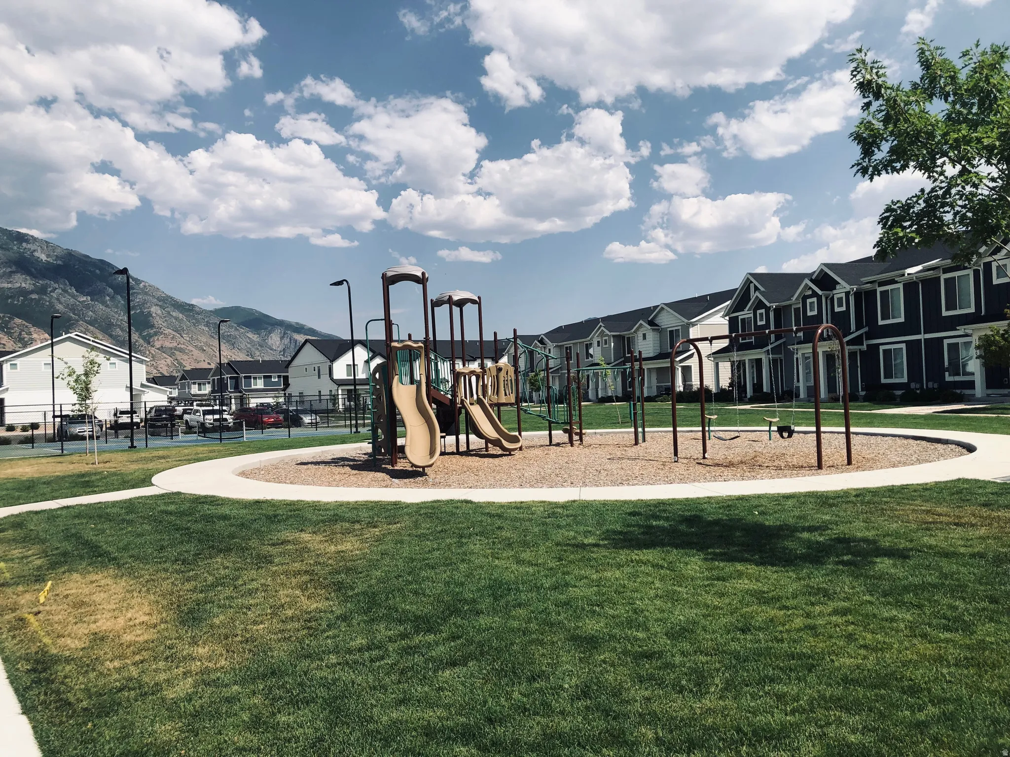Community playground featuring a composite structure with multiple slides and swings, surrounded by a gravel base