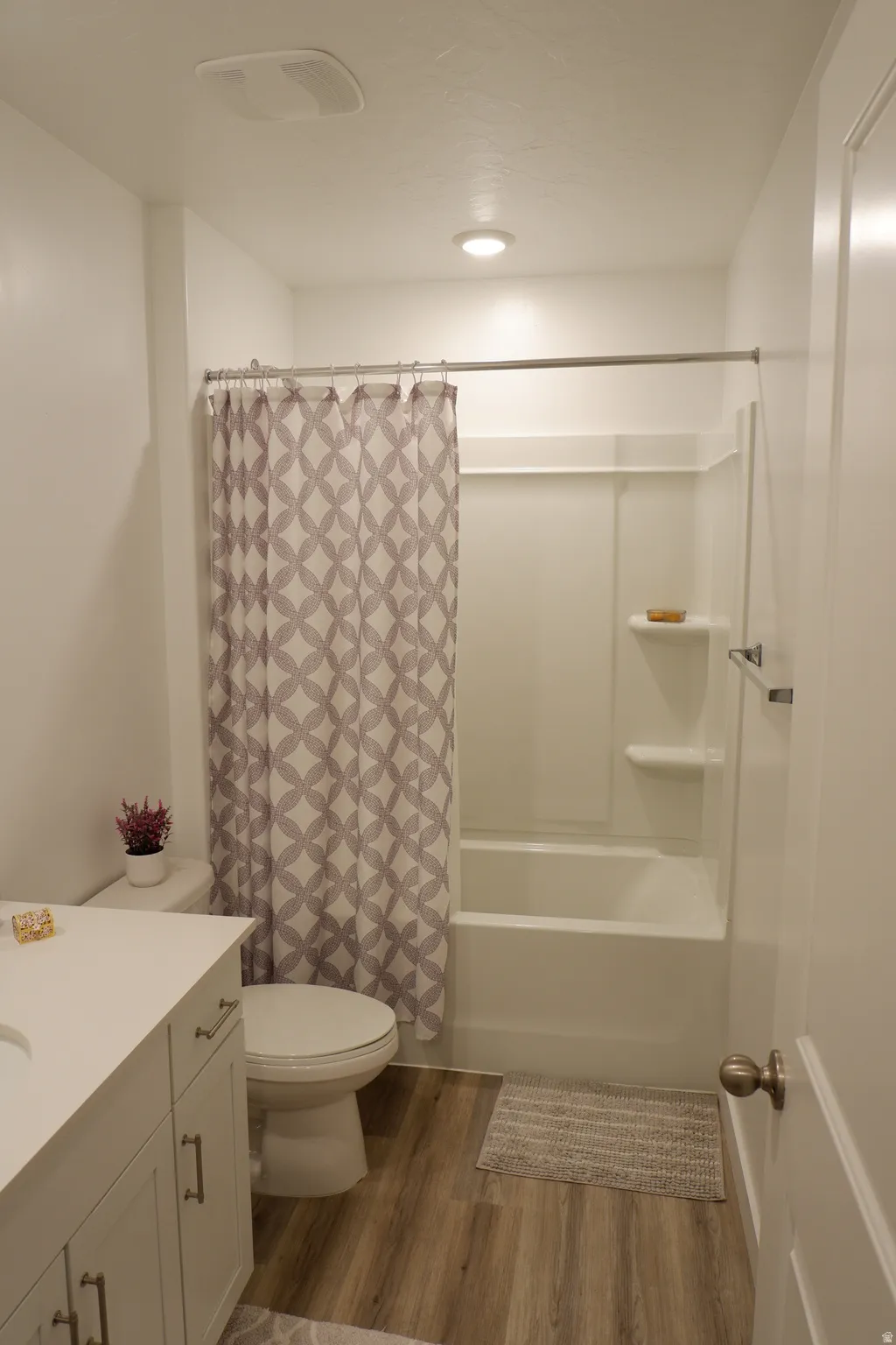 Bathroom featuring wood-finish flooring, a white vanity with an integrated sink and brushed nickel hardware, and a white toilet