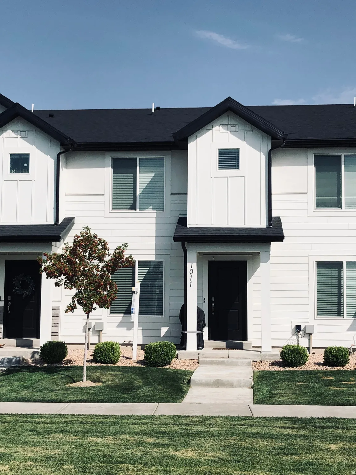 Contemporary townhouse exterior featuring white siding, black trim, and a matching black roof