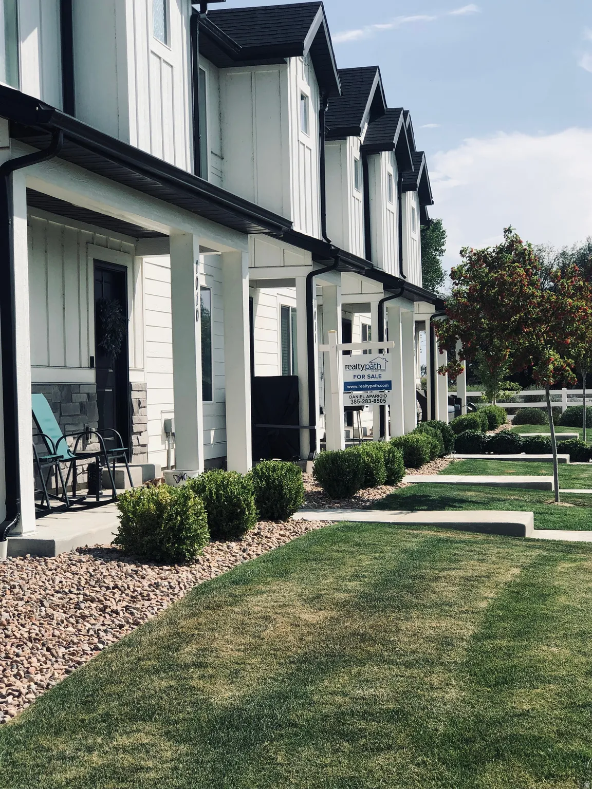 Modern townhome exterior featuring crisp white vertical siding, black trim accents, a black shingled roof, and a covered front porch