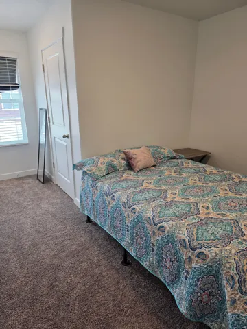 Carpeted room featuring a window with horizontal blinds, a white paneled door, and neutral wall paint