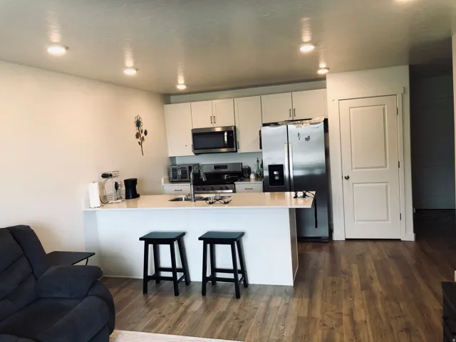 Open-concept kitchen and living area featuring white cabinetry, stainless steel appliances, a white countertop island with seating, recessed ceiling lighting, and wood-finish flooring