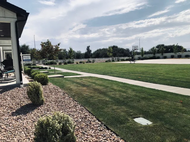 Expansive green space featuring a concrete pathway, a basketball court, and a white fence border