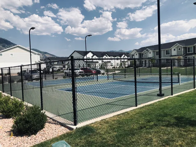 Fenced pickleball court featuring a blue and green playing surface, black chain-link fencing, and overhead lighting fixtures