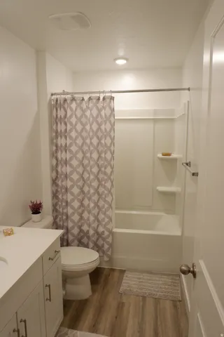 Bathroom featuring wood-finish flooring, a white vanity with an integrated sink and brushed nickel hardware, and a white toilet
