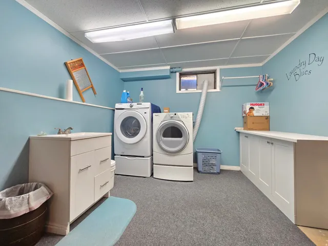 Dedicated laundry room featuring a utility sink with white vanity storage, overhead fluorescent lighting, and a window for natural light