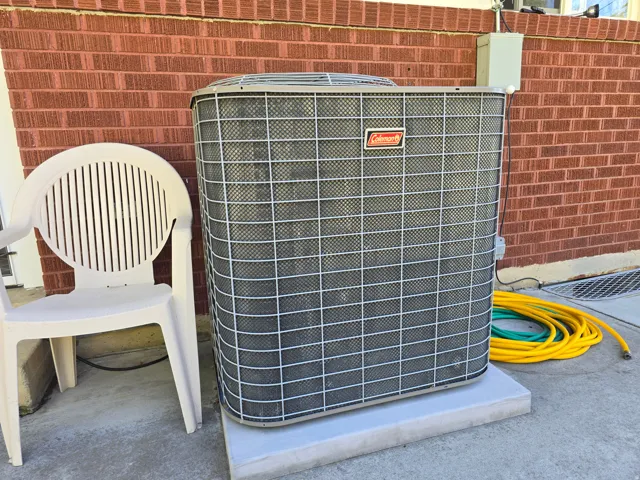 Exterior utility area featuring a Coleman HVAC unit on a concrete pad, against a brick facade