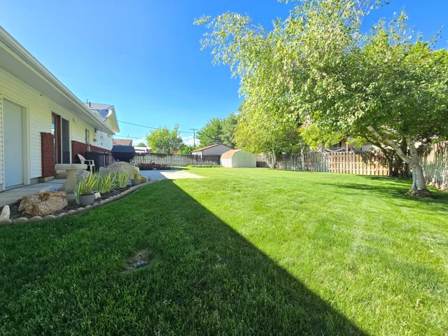 Spacious backyard featuring extensive lawn, mature trees, and a paved patio area