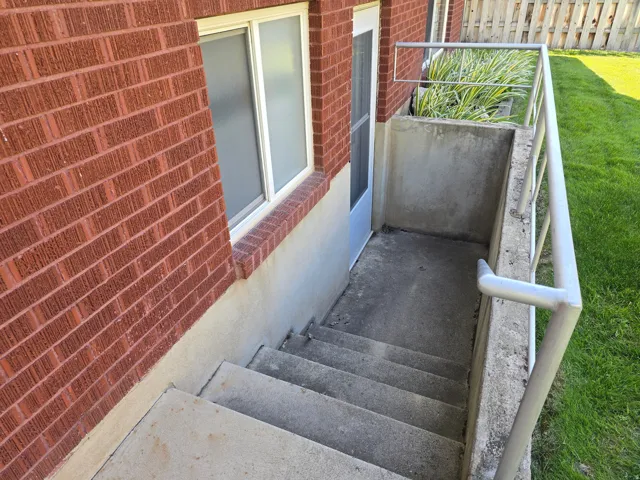 Concrete exterior stairs with metal handrails descend to a white door