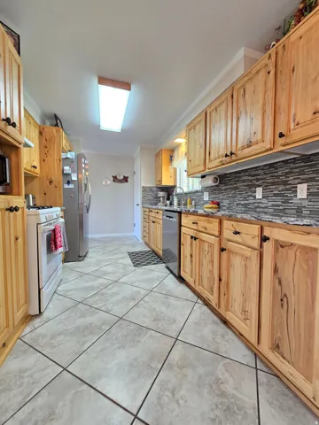 Kitchen featuring extensive wood cabinetry, tile flooring, mosaic tile backsplash, stainless steel dishwasher, and a built-in oven with stovetop