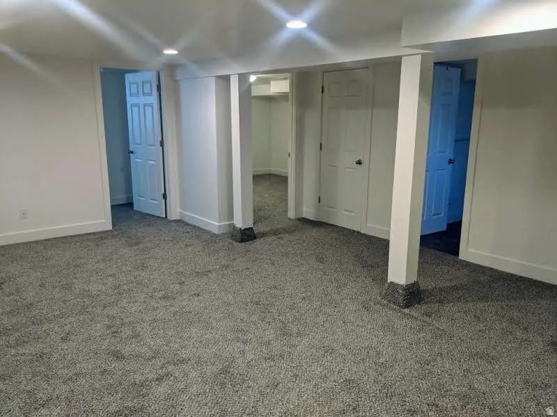 Spacious finished interior area featuring recessed lighting, light gray carpeting, crisp white walls, and multiple paneled doors