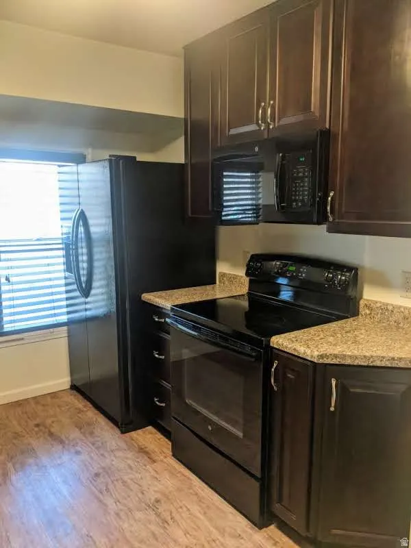 Kitchen featuring dark wood-finish cabinetry with silver hardware, granite-look countertops, black oven with stovetop, black microwave, and black refrigerator