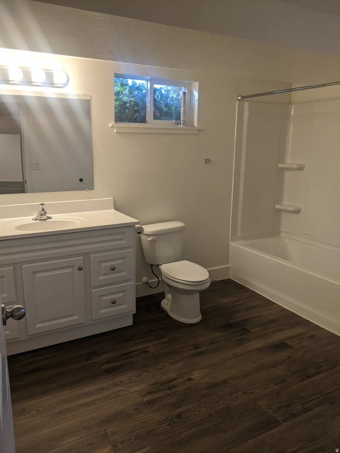 Bathroom featuring a white vanity with integrated sink, wood-finish flooring, and a white tub/shower combination