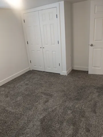 Grey-toned carpeted flooring with white baseboards, featuring a bi-fold closet with panel doors and a white painted interior door