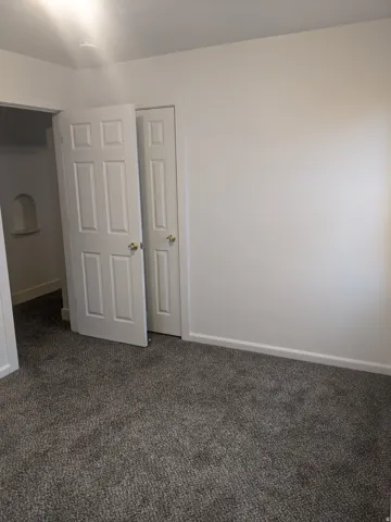Grey textured carpet, white baseboards, and white walls