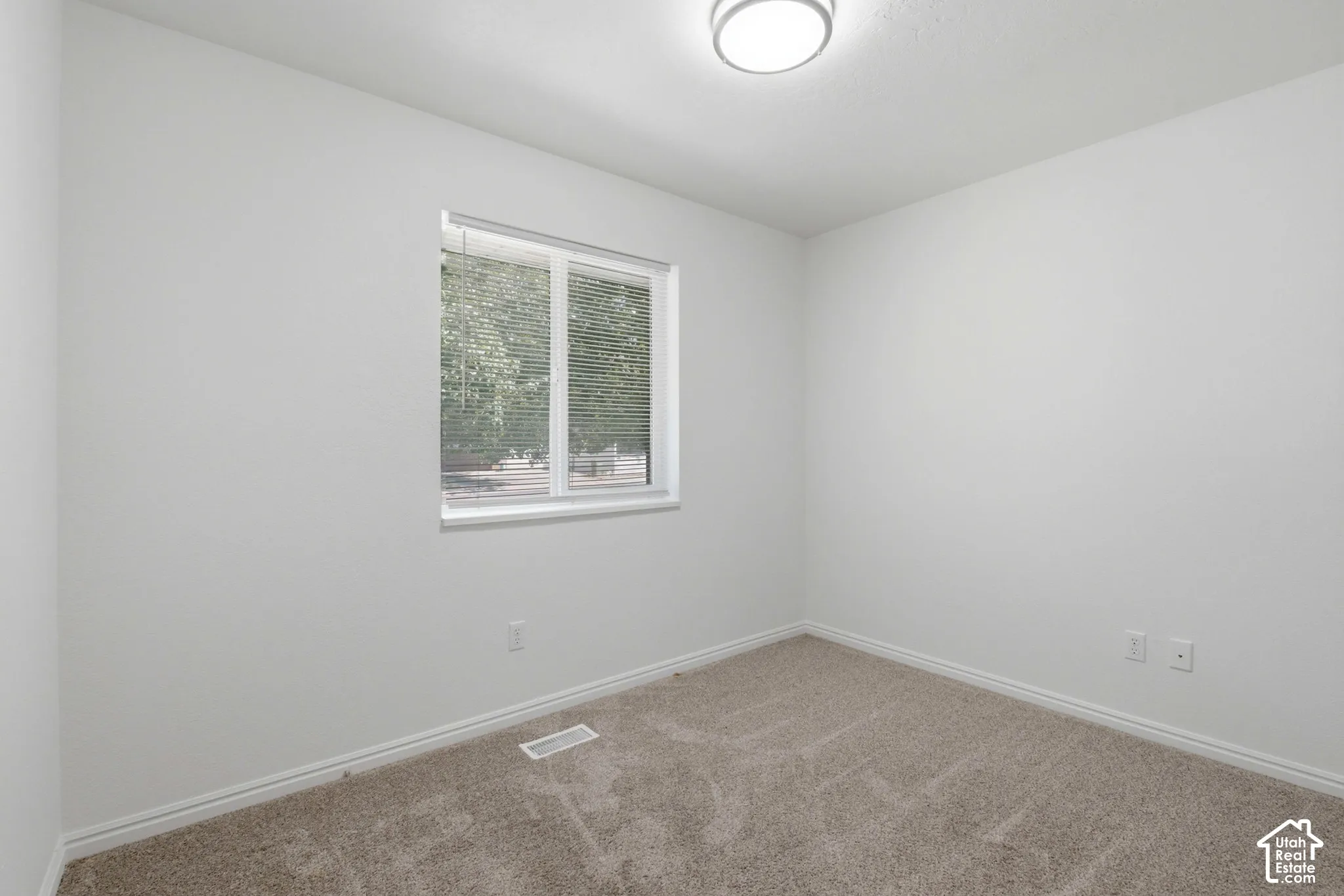 Bright room featuring neutral carpeting, white trim, and a window with blinds