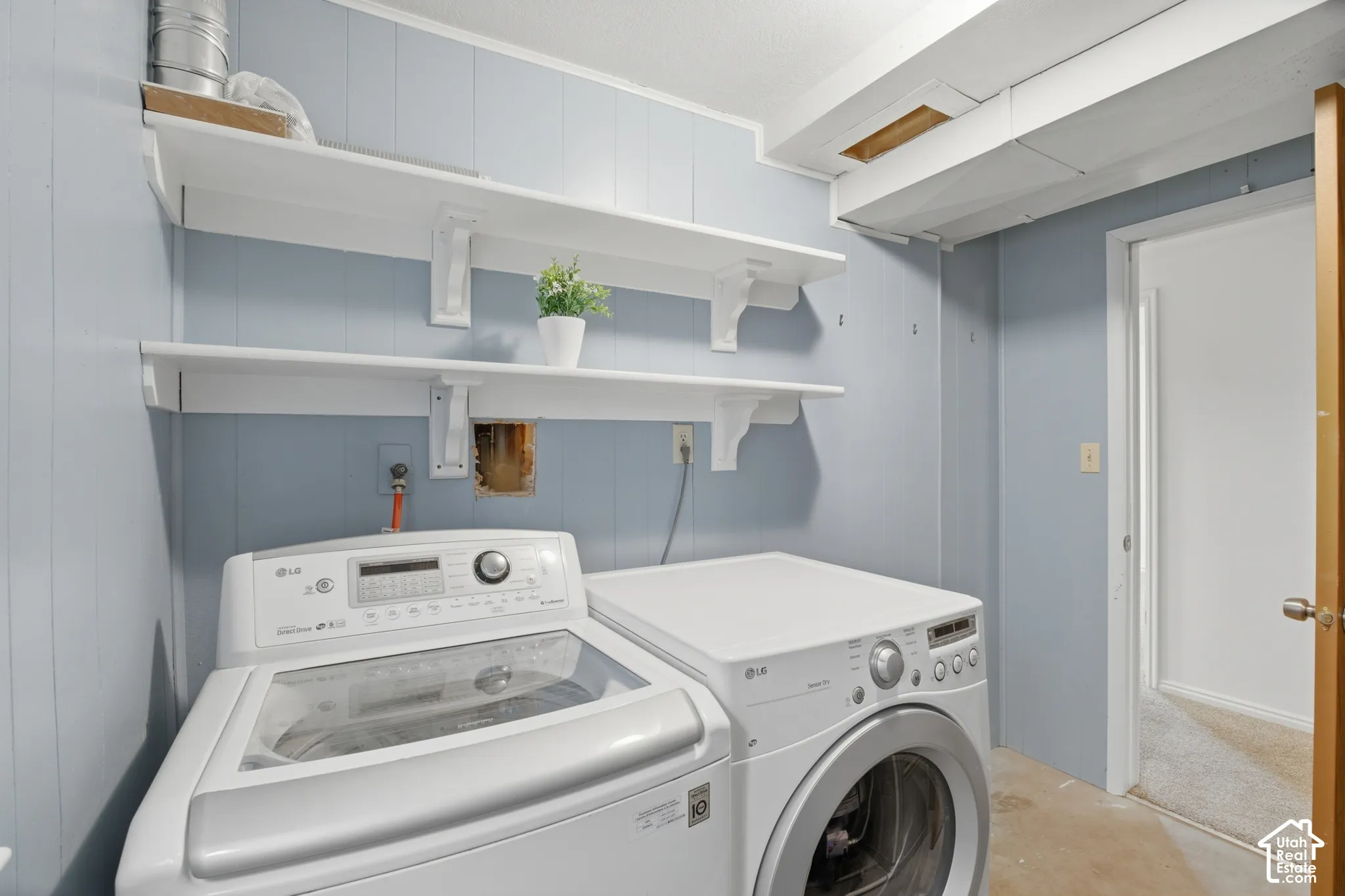 Laundry area featuring wood-paneled walls and a concrete floor
