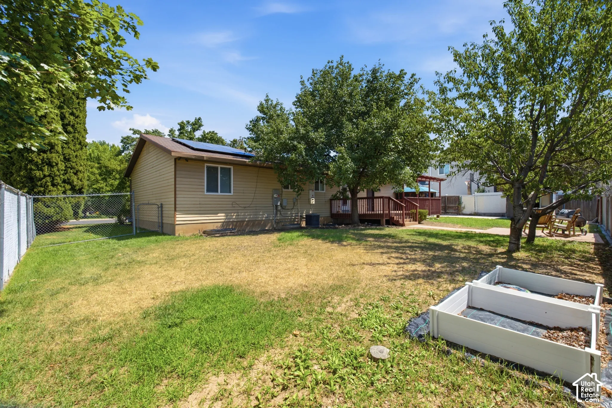 Expansive backyard featuring a wood deck, mature trees, two raised garden beds, and chain link fencing