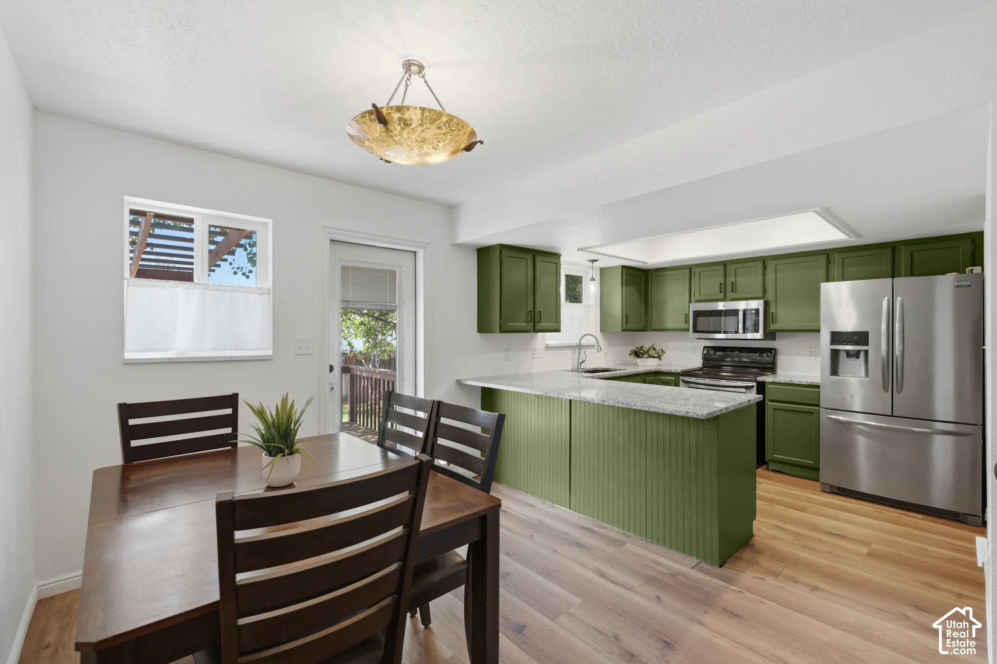 Open-concept kitchen featuring olive green cabinetry, stainless steel appliances, and a central island with a light-toned countertop