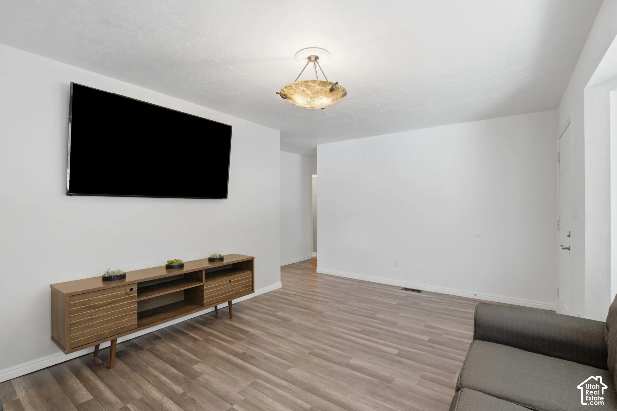 Spacious living area featuring wood-finish flooring, a wall-mounted television, and a decorative ceiling light fixture