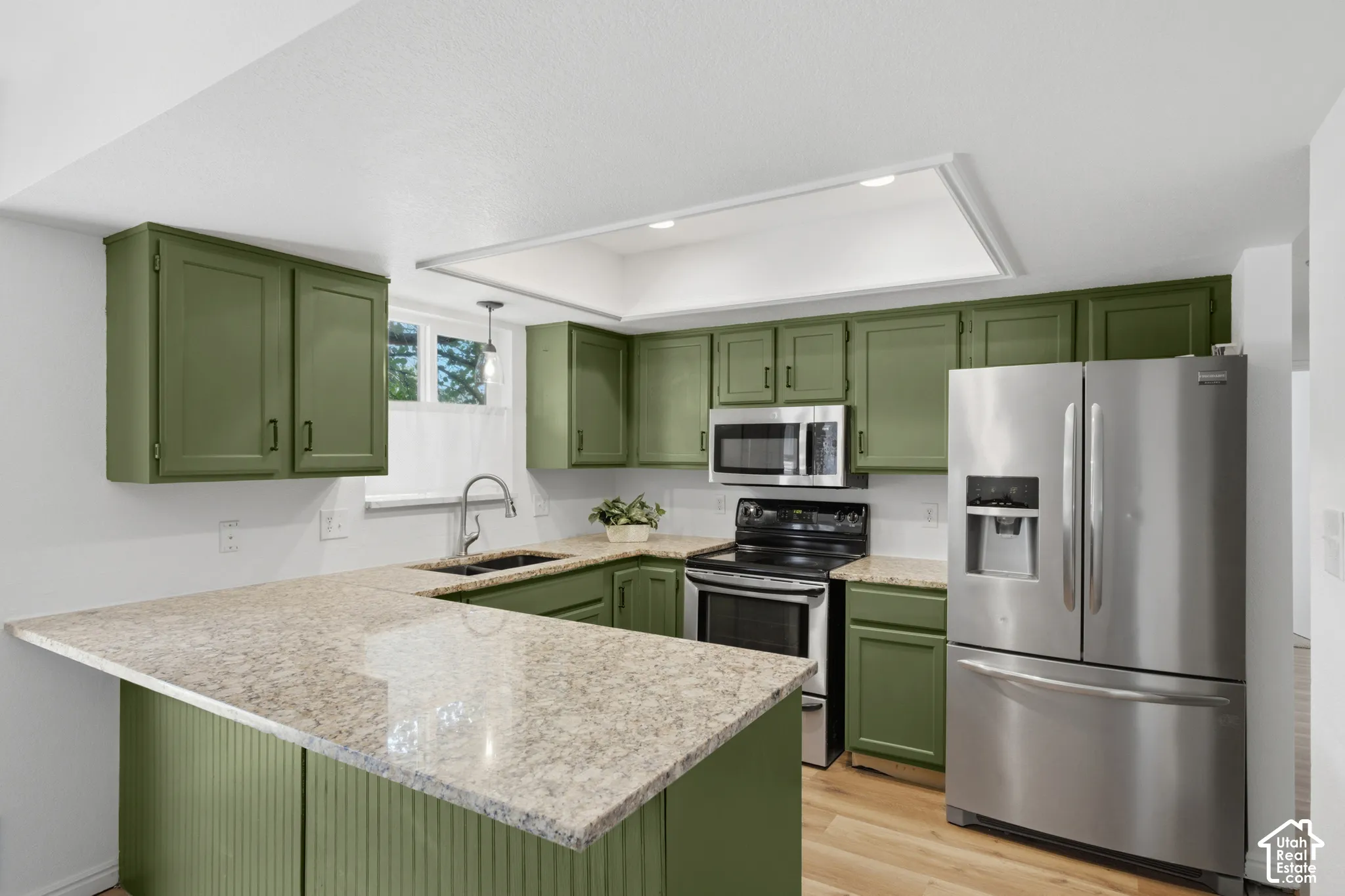 Kitchen featuring green cabinetry, light-toned countertops, stainless steel appliances, and wood-finish flooring
