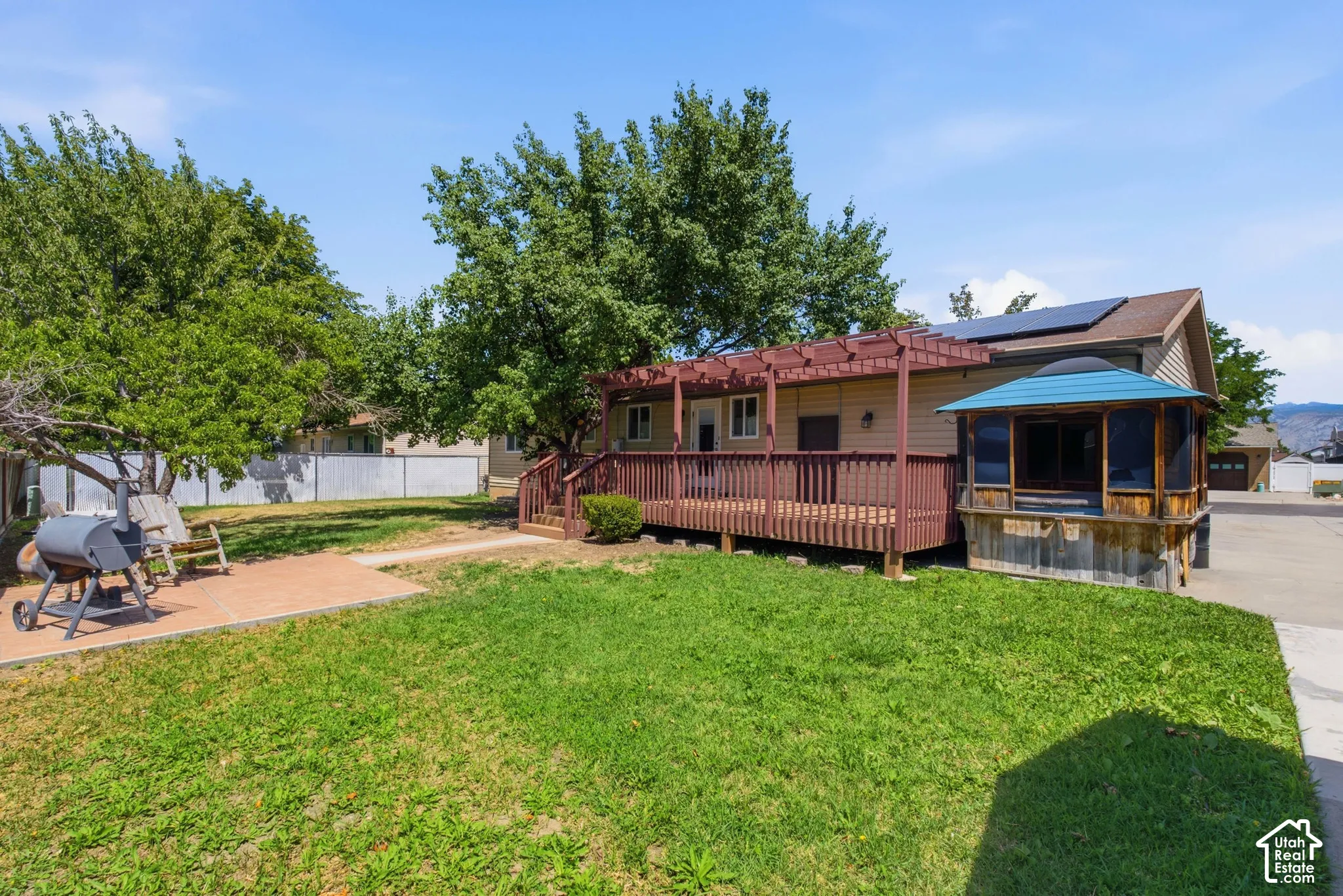 Expansive backyard featuring a manicured lawn, a spacious wooden deck with a pergola, and a built-in screened gazebo