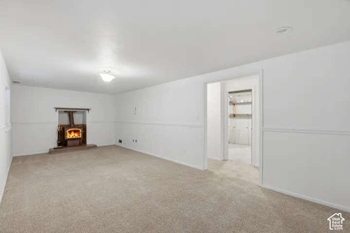 Spacious room featuring a wood-burning stove with a stone hearth, neutral carpet flooring, wainscoting detail, and recessed lighting