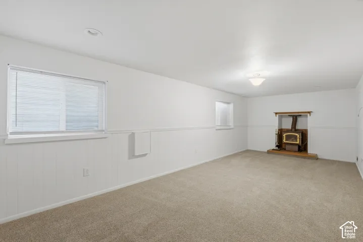 Spacious room with plush carpeting, white wainscoting, and a wood-burning stove set in a traditional hearth