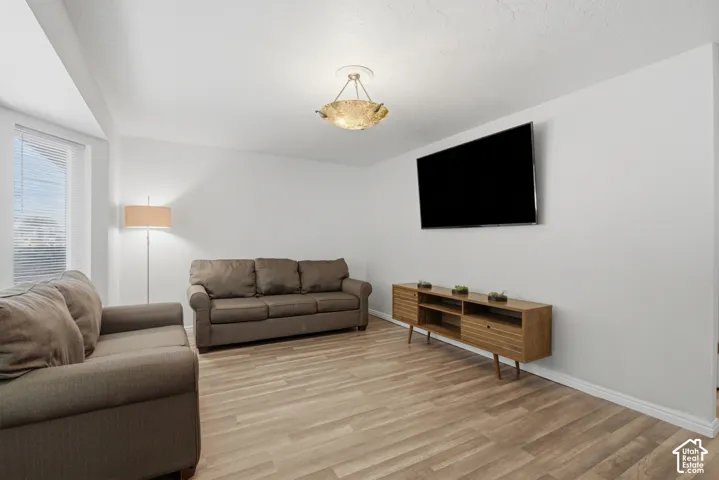 Open room featuring light wood-finish flooring, white walls, and a prominent window with blinds