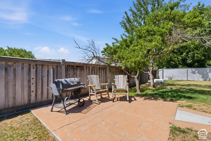 Expansive backyard featuring a red paver patio, wood privacy fencing, and mature trees providing natural shade