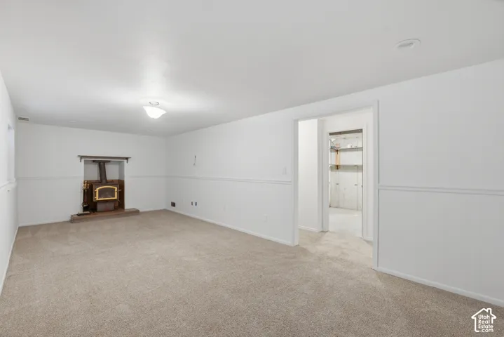 Spacious room featuring neutral carpeting, white walls with wainscoting, and a wood-burning stove within a recessed hearth