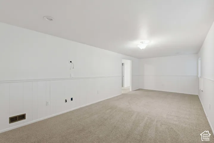 Spacious room featuring neutral carpeting, white walls, and wainscoting
