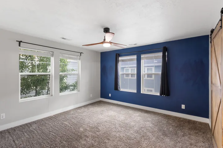 Carpeted room featuring a ceiling fan, four windows, and a barn door