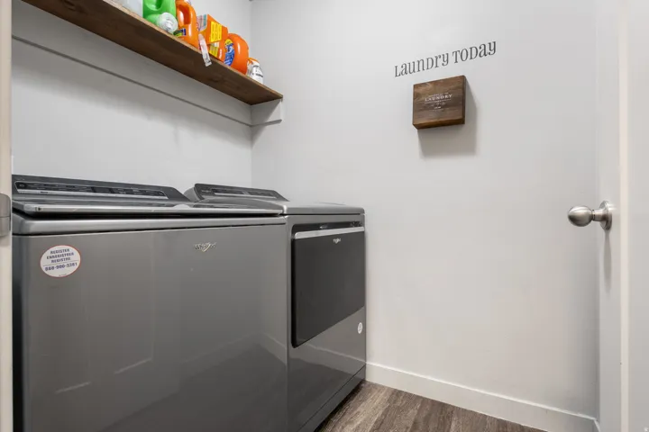Dedicated laundry area featuring wood-finish flooring, a floating wood-finish shelf, and neutral wall tones