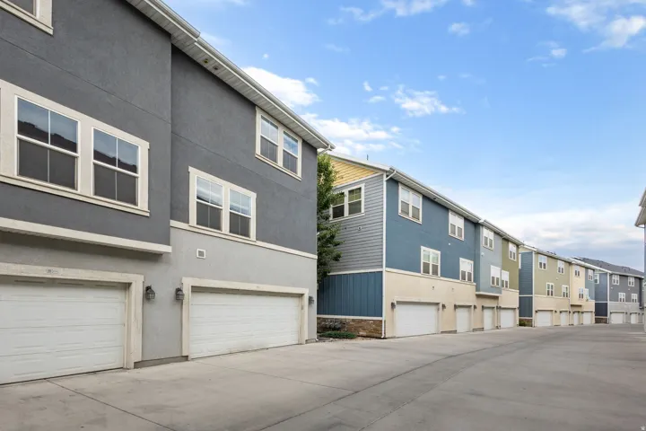 Modern townhome exteriors featuring two-tone stucco and siding, white-trimmed windows, individual garage access, and an expansive paved driveway