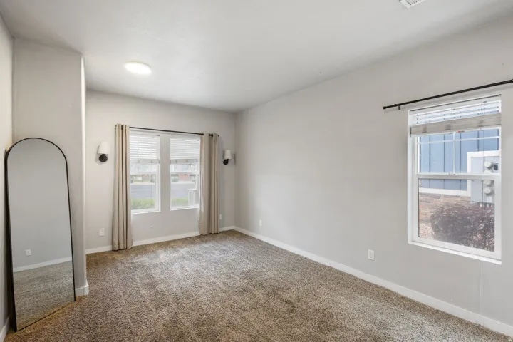 Spacious room featuring neutral carpeting, light gray wall paint, and two distinct window placements