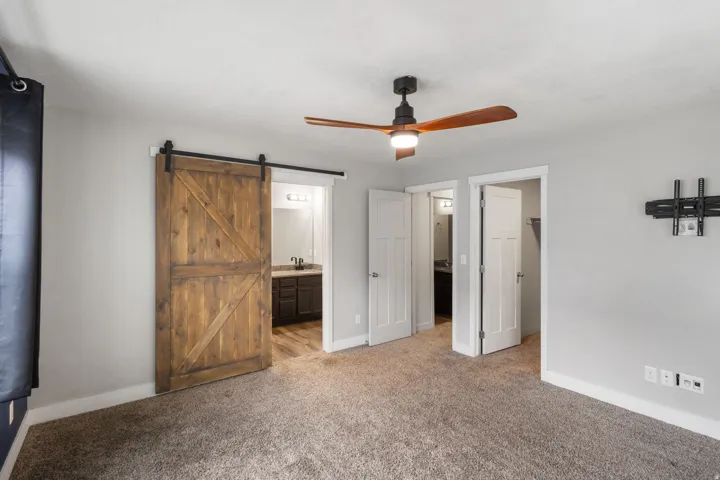 Bedroom featuring a wood-finish barn door, ceiling fan with wood-finish blades, and neutral gray walls