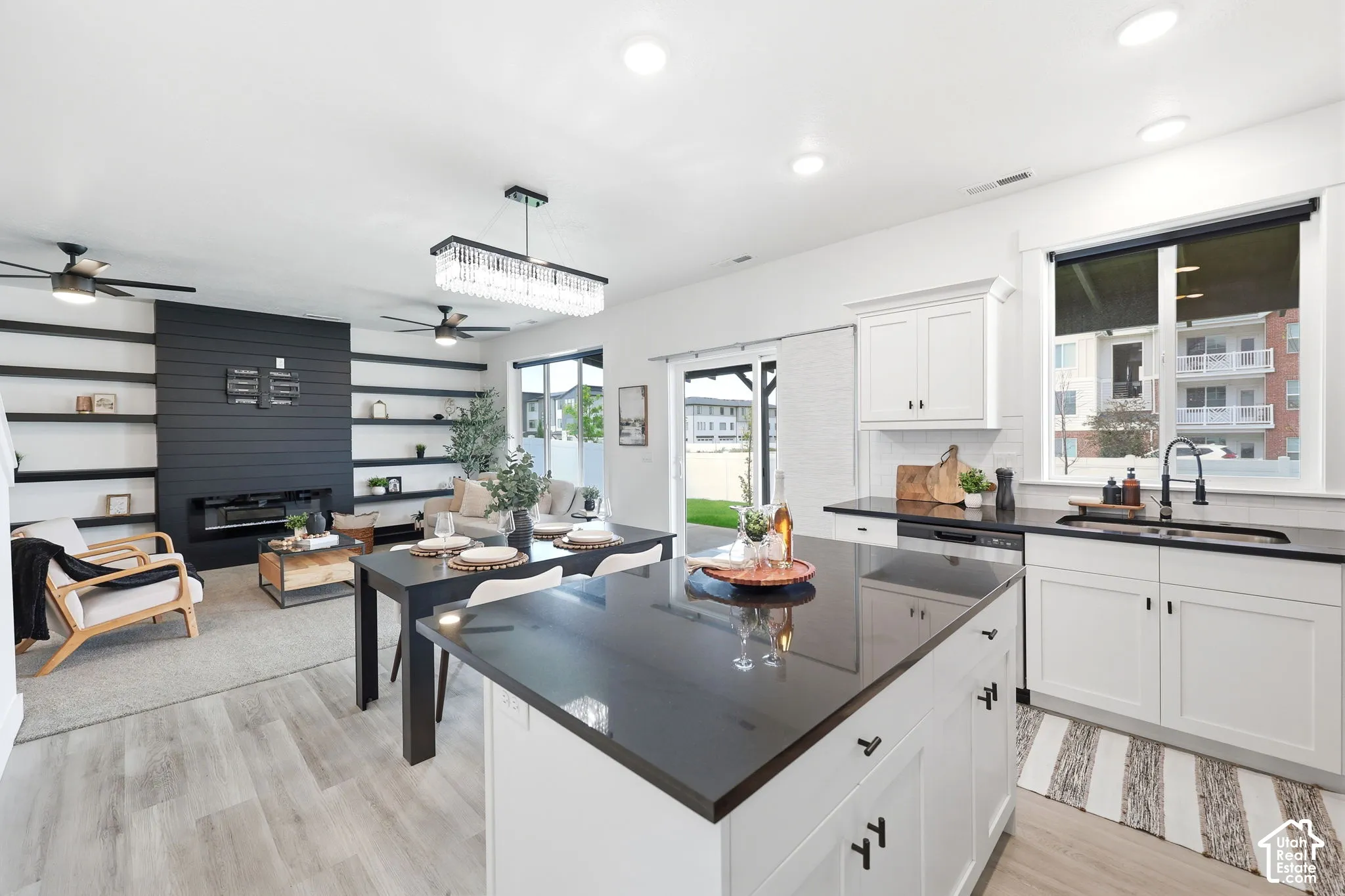Open-concept kitchen and living area featuring white cabinetry, dark countertops, wood-finish flooring, a built-in fireplace, and a sliding glass door to the exterior