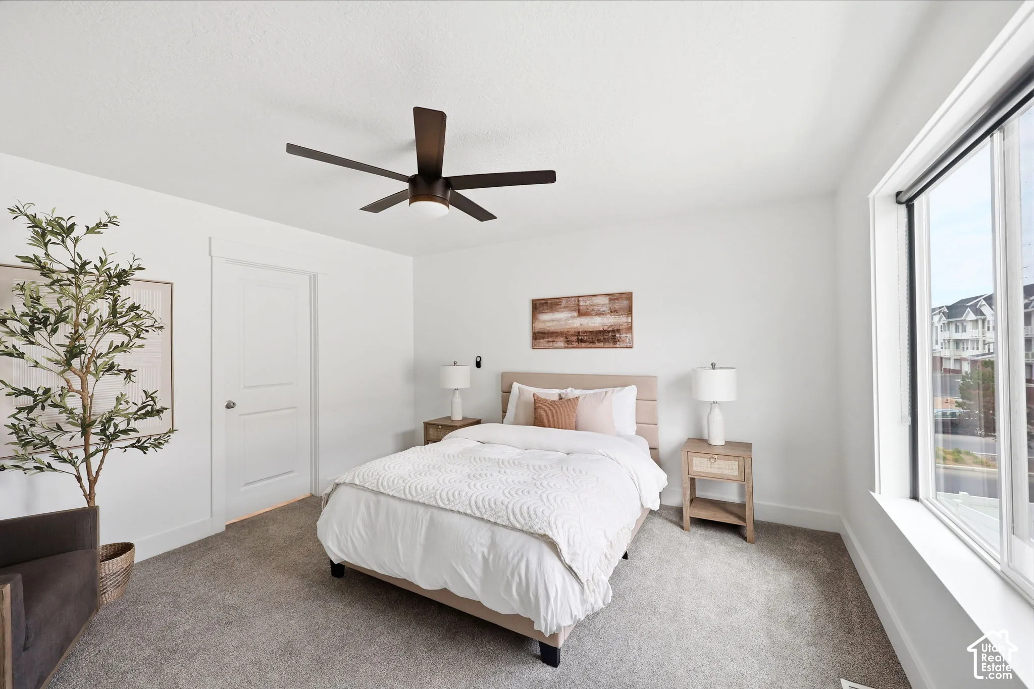 Bedroom featuring a contemporary ceiling fan, white trim, a solid door, and a large window with roller shades