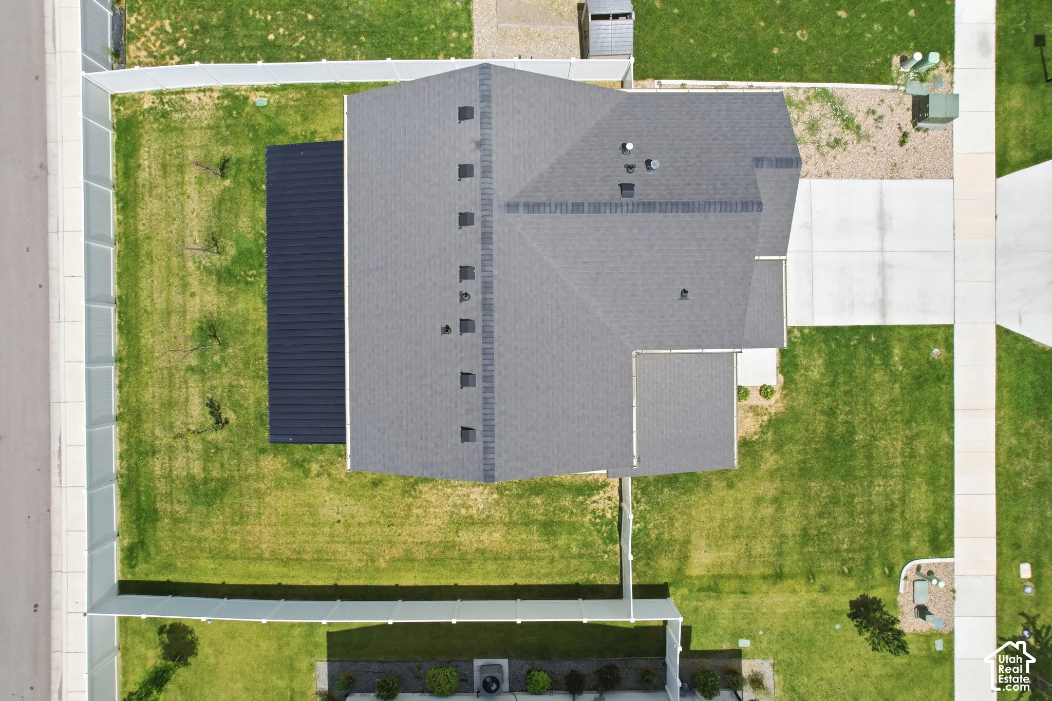 Property featuring a dark shingle roof, expansive green lawn, concrete driveway, and a fenced perimeter