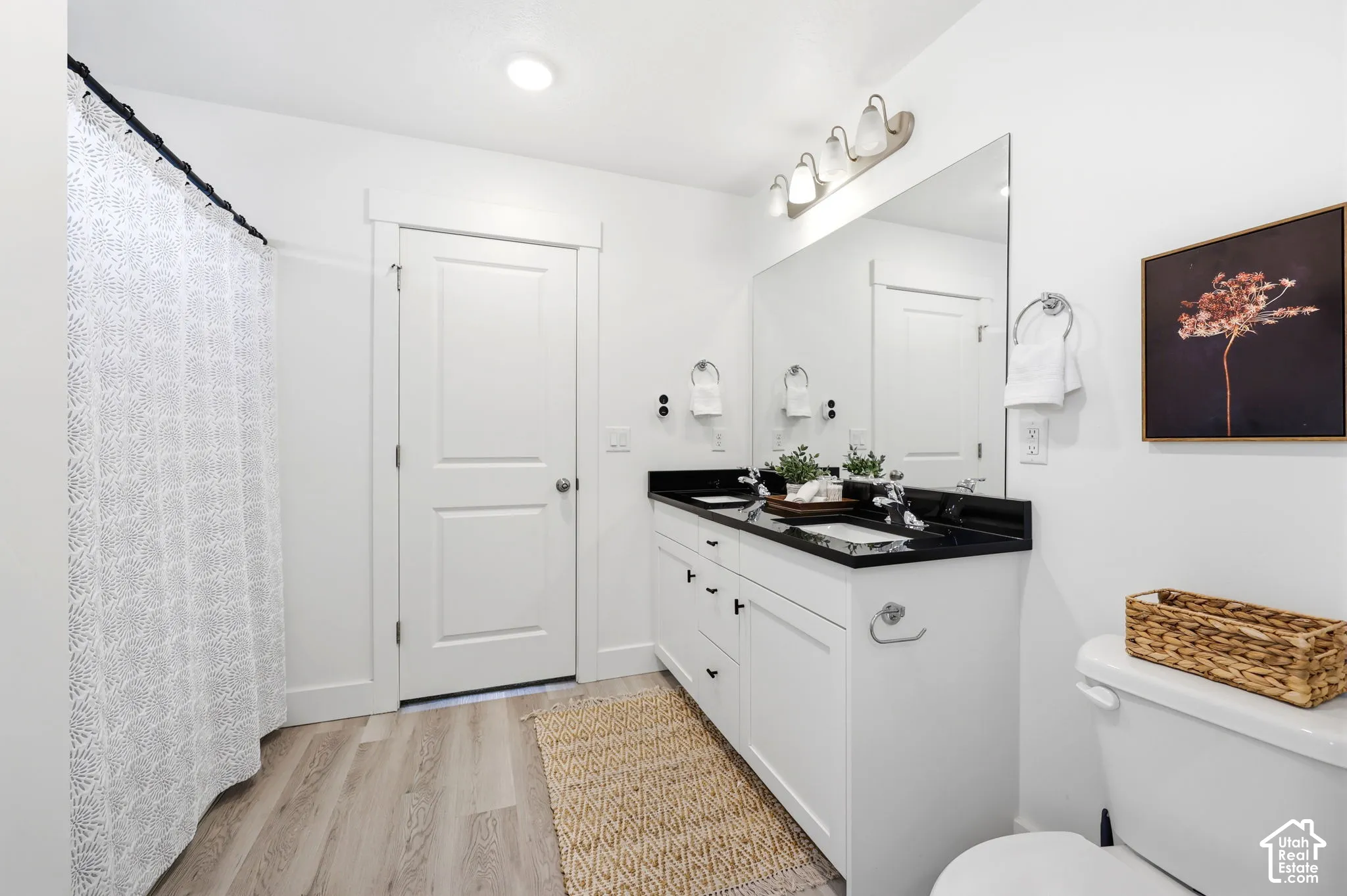 Bathroom featuring a double vanity with black countertops, white cabinetry, and brushed nickel hardware