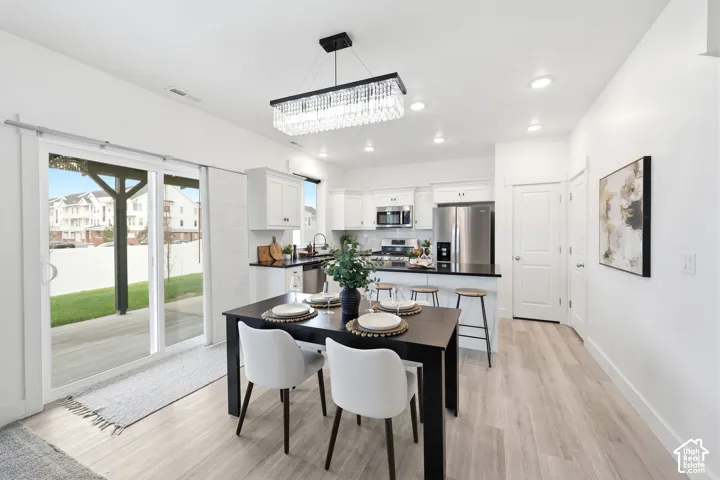 Open-concept dining area featuring light wood-finish flooring, a contemporary chandelier, and recessed lighting