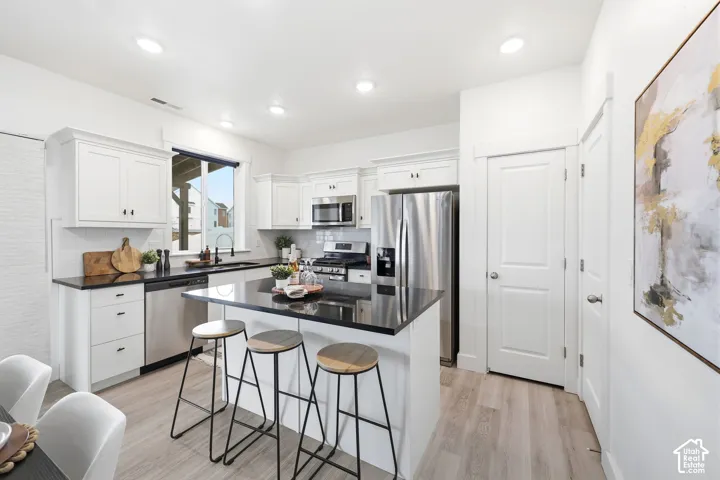 Modern kitchen featuring white shaker cabinetry, stainless steel appliances, dark countertops, and wood-finish flooring