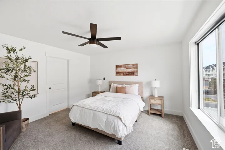 Bedroom featuring a contemporary ceiling fan, white trim, a solid door, and a large window with roller shades