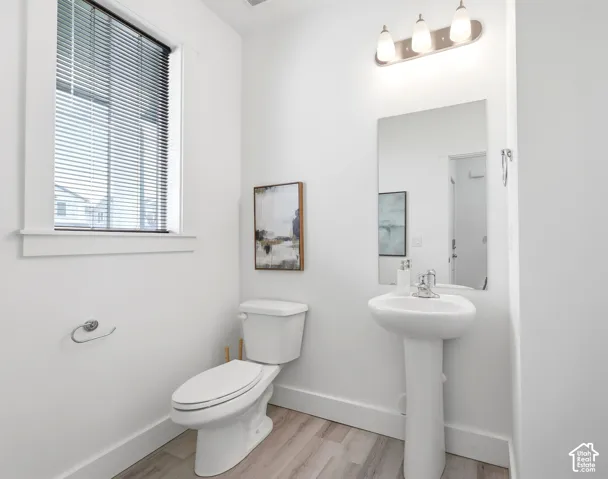 Bathroom featuring a pedestal sink, wall-mounted mirror, three-light vanity fixture, and wood-finish flooring