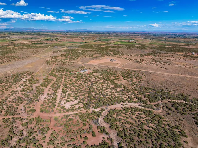 Expansive natural landscape with scattered vegetation, visible road network, and distant rural scenery under a blue sky
