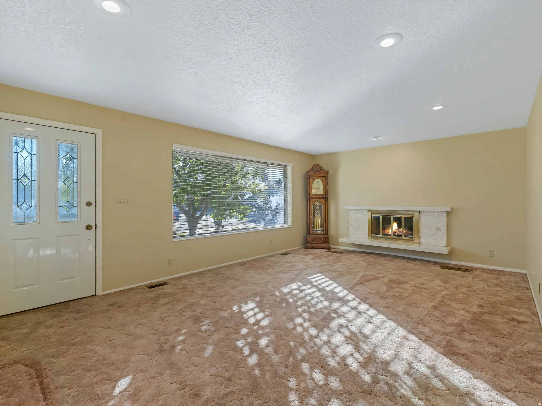 Living area featuring a white entry door with decorative glass inserts, a wide window with horizontal blinds, a fireplace with a light-colored surround, and recessed ceiling lighting